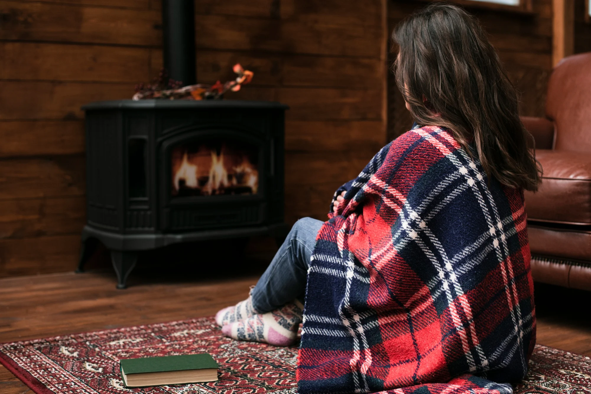 Vrouw met een plaid bij een houtkachel