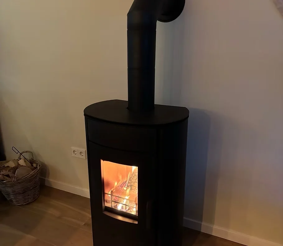 Zwarte houtkachel brandend, met verticale afvoer naar de wand