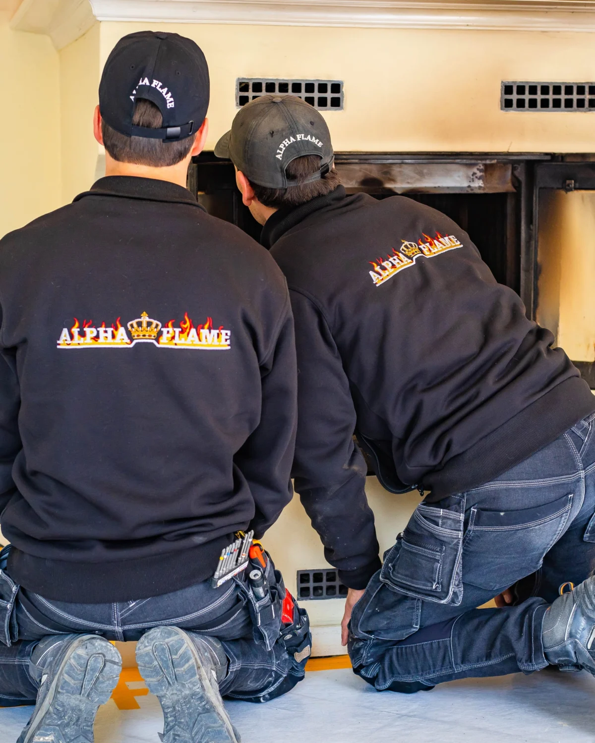 Twee monteurs van Alpha Flame geknield voor een geopende inzethaard