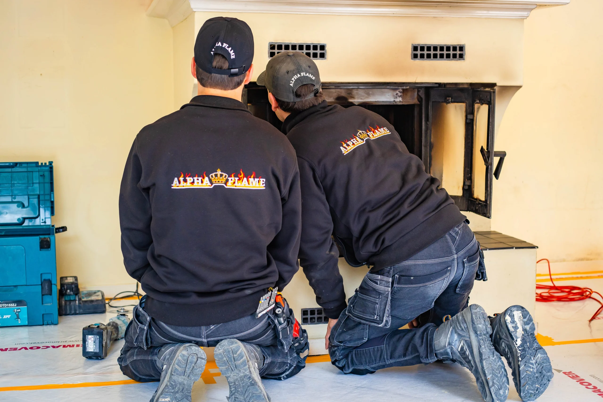 Twee monteurs van Alpha Flame geknield voor een geopende inzethaard